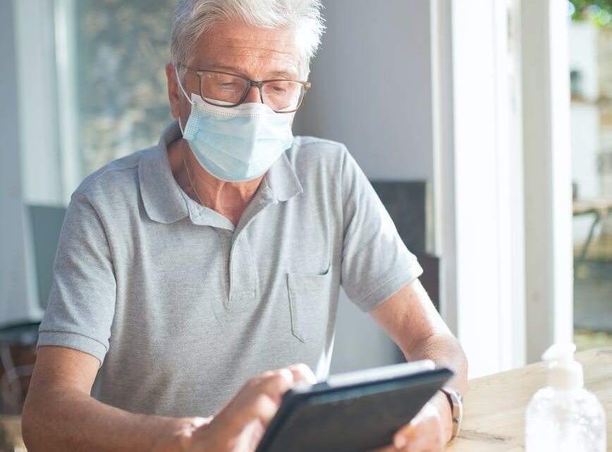 elderly man wearing face mask using a tablet