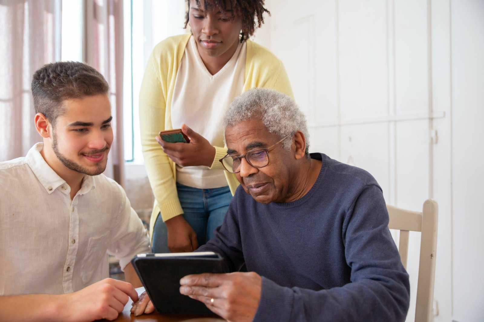 an elderly man in blue sweater holding a tablet while talking to the people beside him