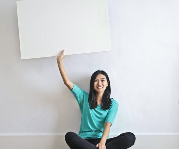 smiling ethnic woman with blank poster in empty flat
