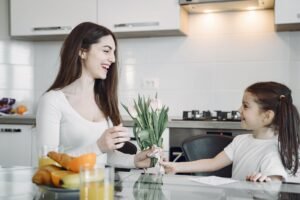 happy girl presenting flowers to mother on kitchen