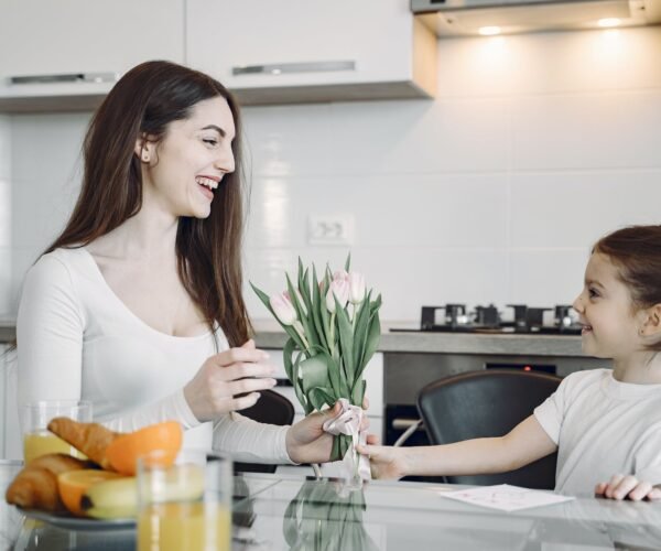happy girl presenting flowers to mother on kitchen